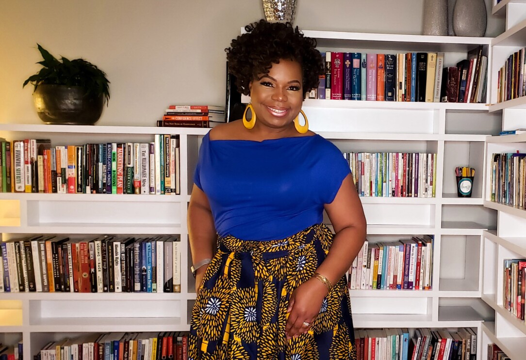 An image of a woman smiling for a photo in front of her bookcase.