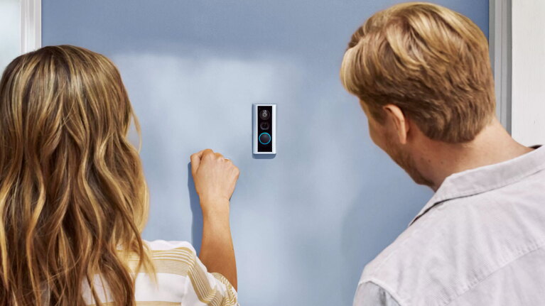 an image of two people knocking on a door. There is a Ring Peephole Camera in the middle of the door.