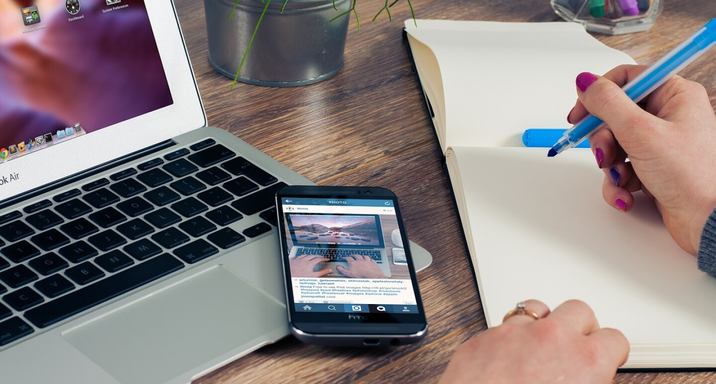 Picture of a laptop and a notepad with a lady's hand holding a pen against a notepad