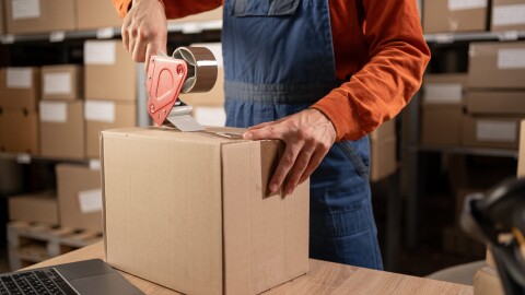 Worker sealing cardboard box with packing tape in warehouse
