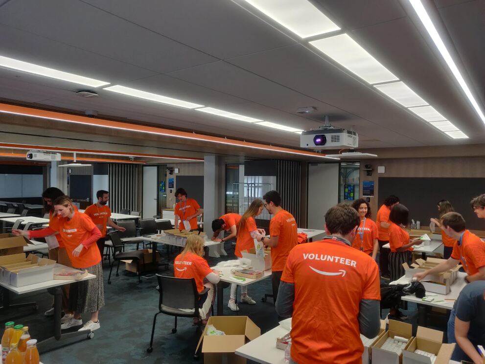 Amazon Mitarbeiter:innen in Frankreich in orangenen Volunteer T-Shirts stellen Produkte für Spenden zusammen.