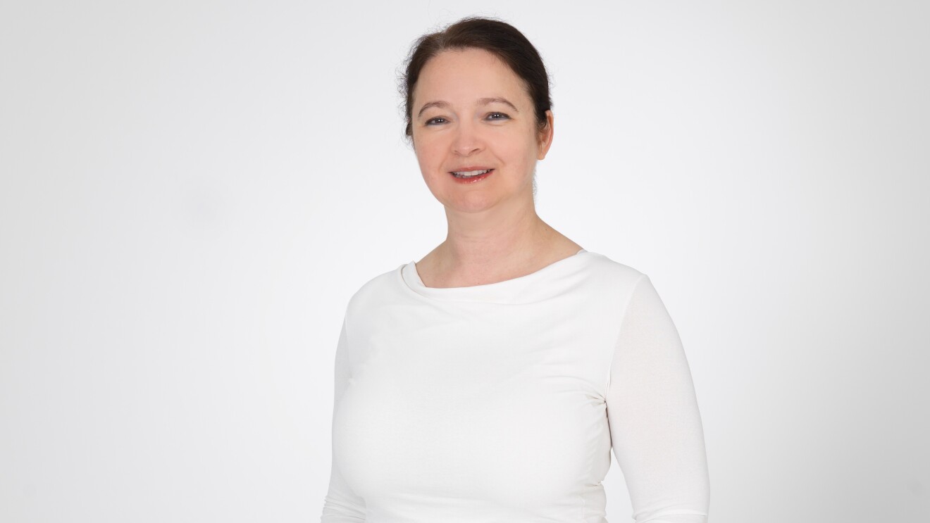 AWS Mitarbeiterin Agnes Balazs mit weißem Oberteil vor einer weißen Wand stehend.