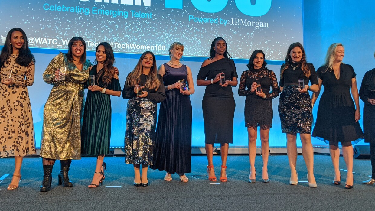 Women in tech award winners on stage with their awards. They are standing in front of a projection reading TechWomen100