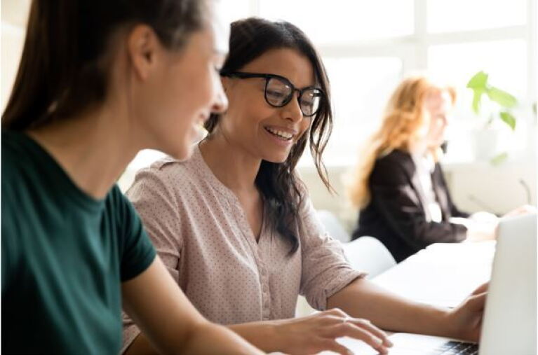 zwei junge Frauen sitzen vor dem Computer und besprechen sich