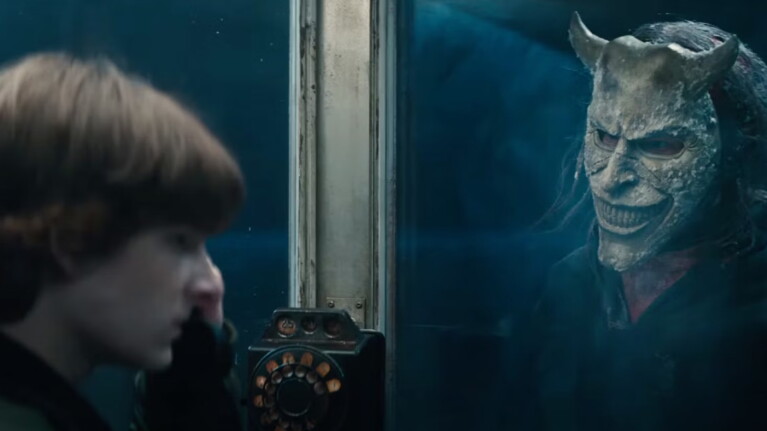 Boy on a black phone with a man in a mask next to him behind a glass wall
