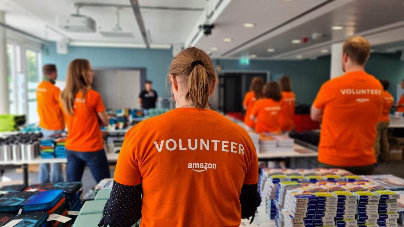 Amazon Mitarbeiterin in einem T-Shirt mit der Aufschrift "Amazon Volunteer" an einem Packtisch.