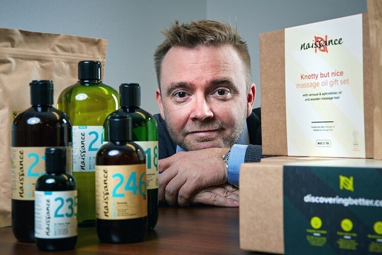 Man dressed in a suit, positioned behind bottles and cardboard boxes 