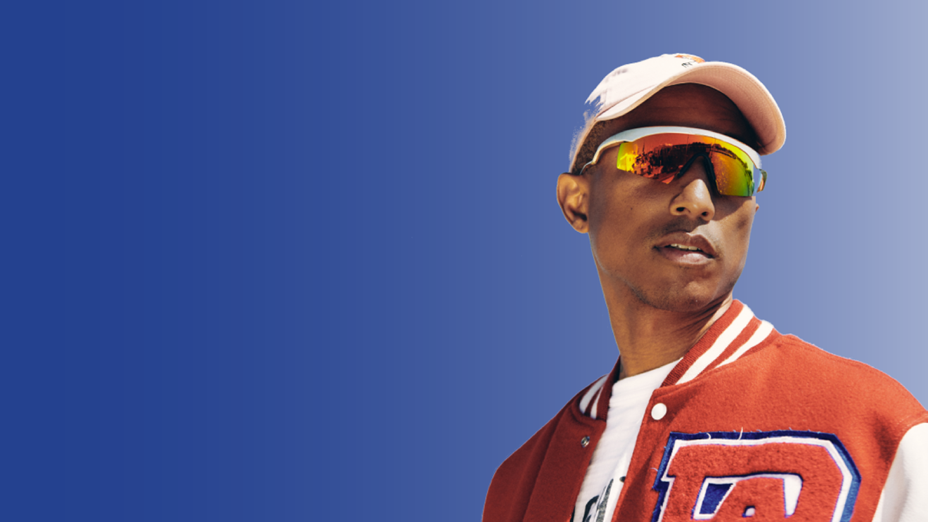 艺术家法瑞尔·威廉姆斯眺望远方的照片。他穿着红白相间的夹克,戴着白色棒球帽,戴着偏光太阳镜。他身后有一个深蓝色的背景,逐渐变成浅蓝色。