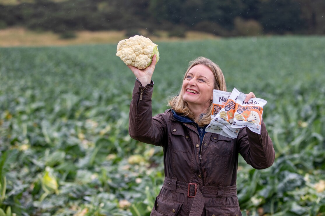 Business owner holding up a cauliflower and nudie snacks