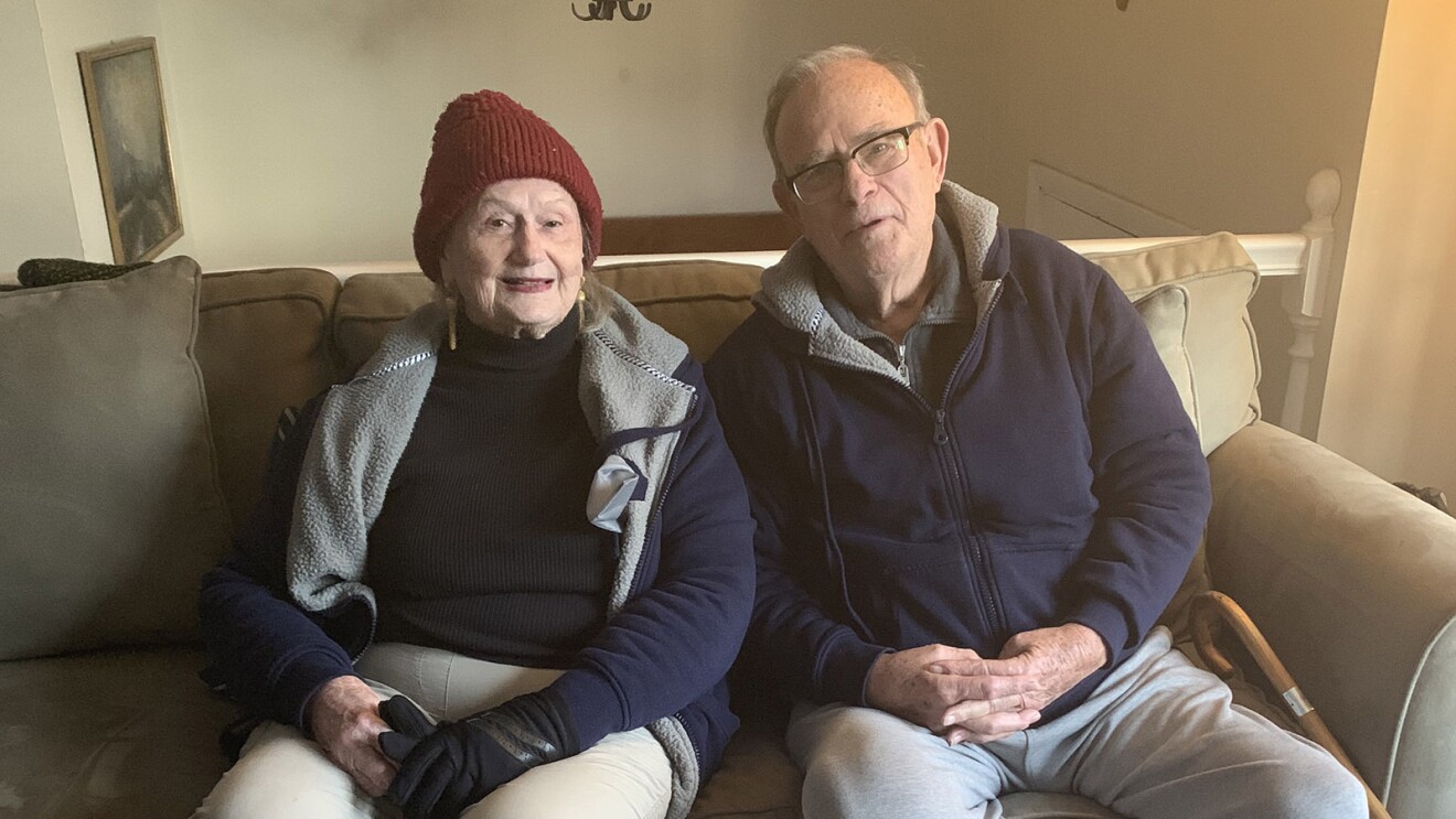 An image of a man and a woman sitting on a couch in their home, smiling for a photo.