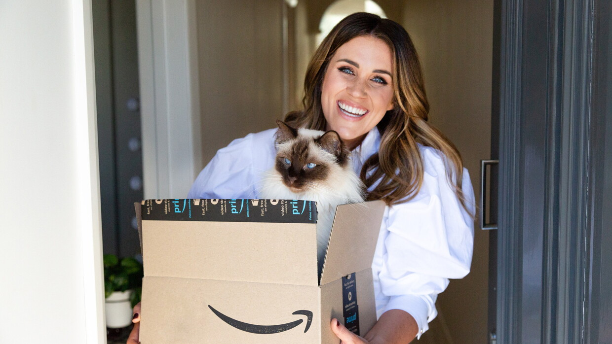 A television personality who is a woman holds her Siamese cat and smiles at the camera