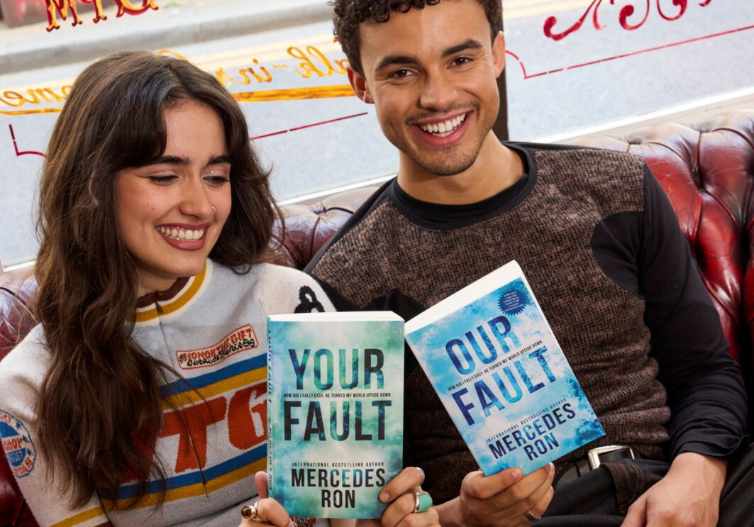Smiling actors holding books titled 'Your Fault' and 'Our Fault' by Mercedes Ron