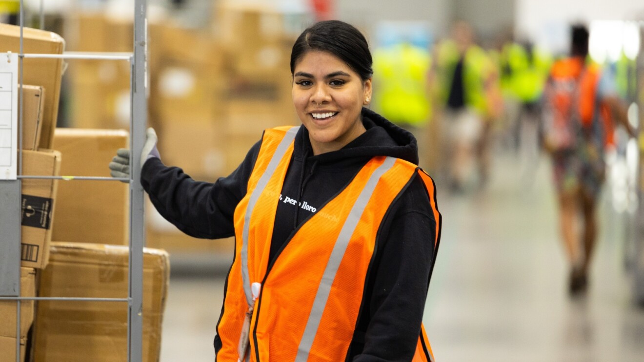 Woman in black hoodie and orange safety vest standing by Amazon packages