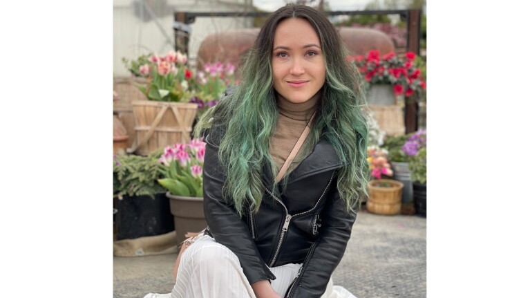 An image of a woman smiling for a photo while sitting in front of a garden of potted flowers.