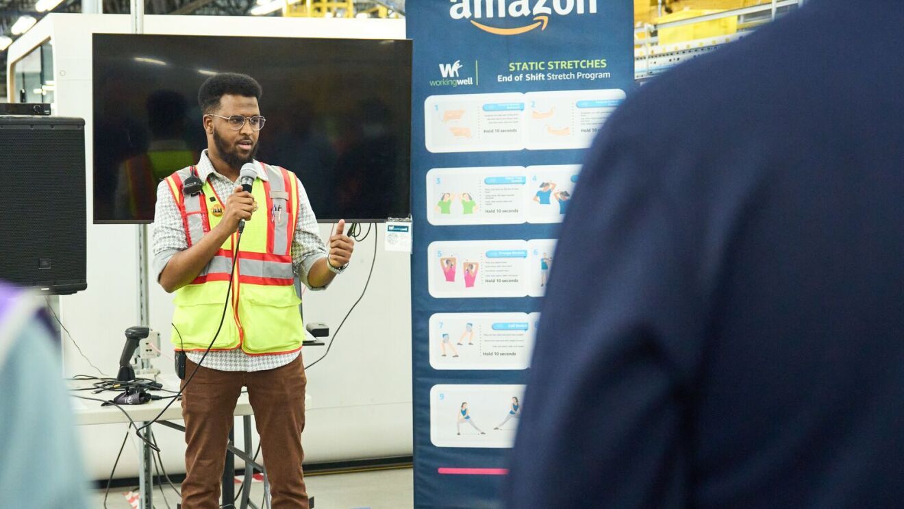 An image of Abdiaziz, an area manager working in an Amazon fulfillment center, talking to employees.