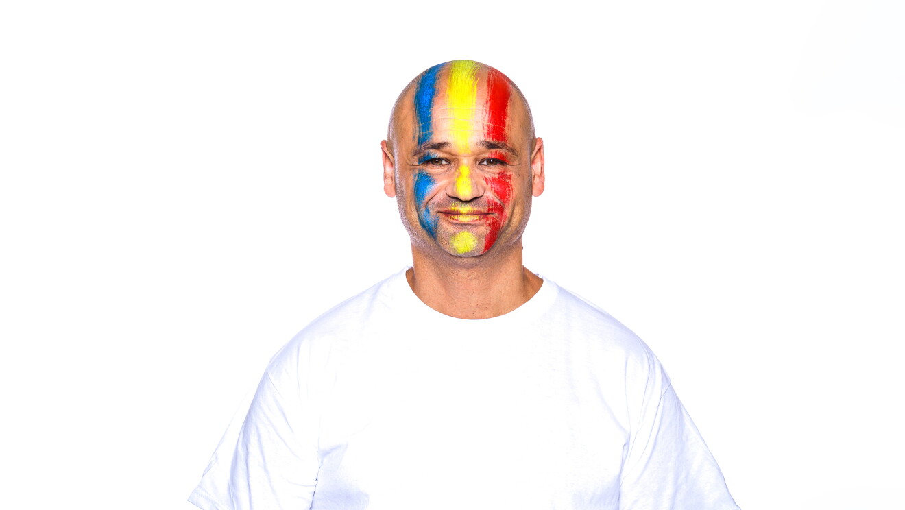 Para el Día de la diversida Amazon ha preparado una acción con asociados de diferentes países que llevan la bandera pitnada en su cara. En la foto, Adrian con camiseta blanca, mirando sonriendo a cámara con la bandera de su país puntada en la cara. No tiene pelo ni barba.