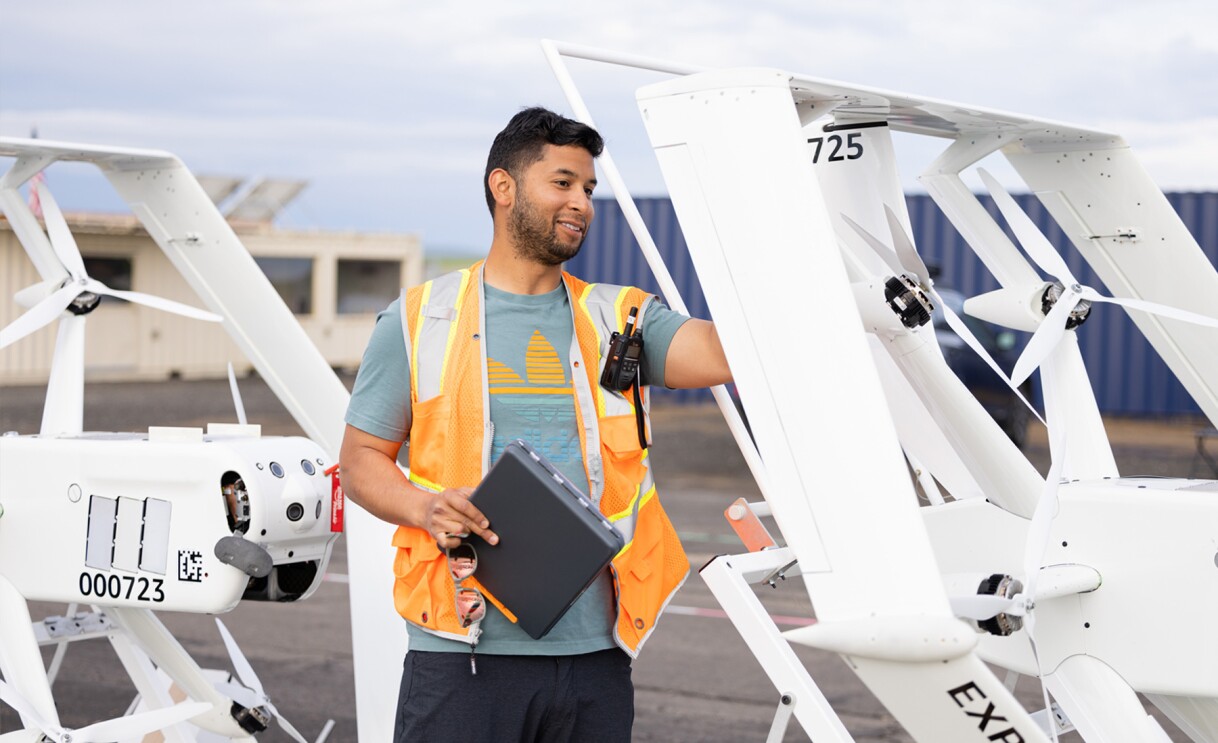 Images of Amazon employees wearing orange safety vests work on drones.