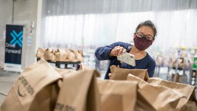 A woman wearing a mask and glasses uses her smartphone to scan Prime Now delivery bags.