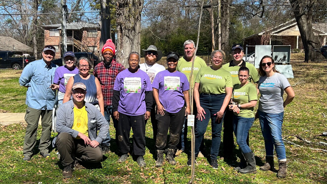 Group of diverse volunteers in Amazon and community shirts gathered for outdoor project