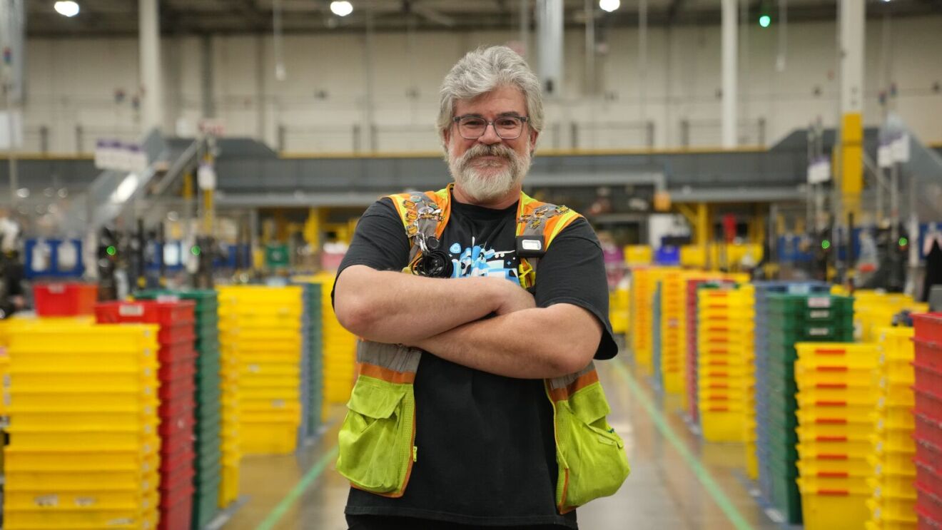 Amazon employee wearing glasses and yellow safety vest standing among stacked containers