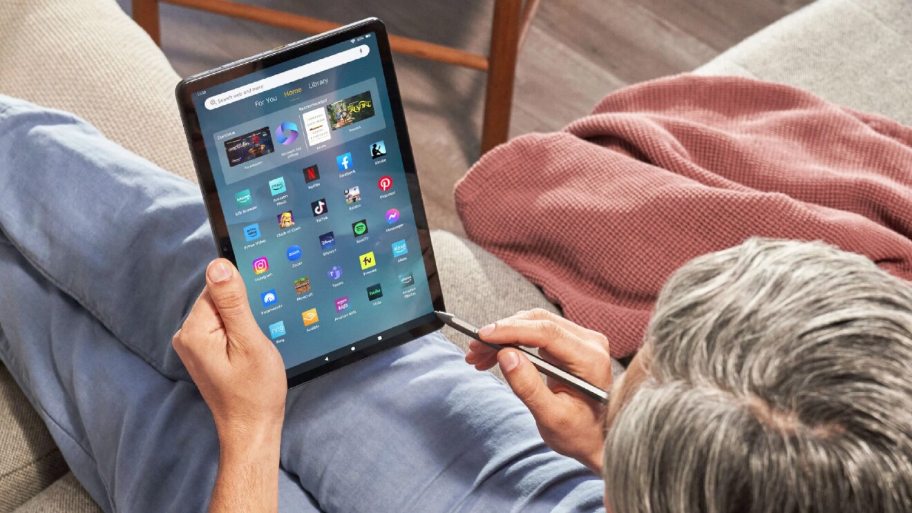 Prime Day 2023 live blog best deals: man using a Fire tablet and pen while sitting on the couch.