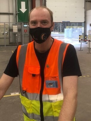 Alex Van Krimpen, temporary operations supervisor at Amazon's delivery station in Penrith pictured on the shop floor wearing a high visibility vest and a black face mask.