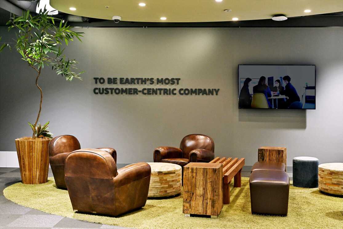 グレーの壁に文字のプレートが貼られている。その横にテレビモニター。その前に茶色の皮張りのソファーが置かれている