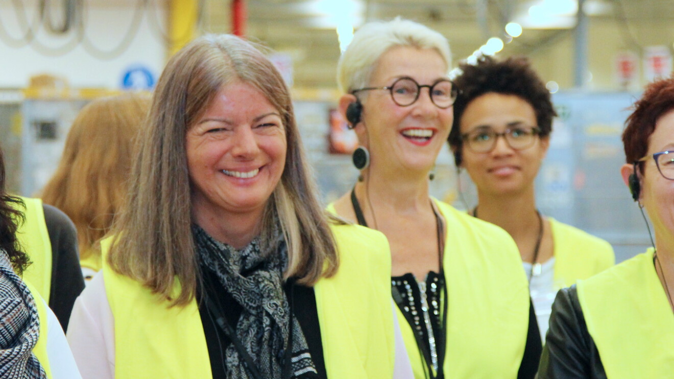 Eine Gruppe von Frauen in Sicherheitsweste blickt freundlich in die Kamera. Im Hintergrund ist das Lager in Pforzheim zu sehen.