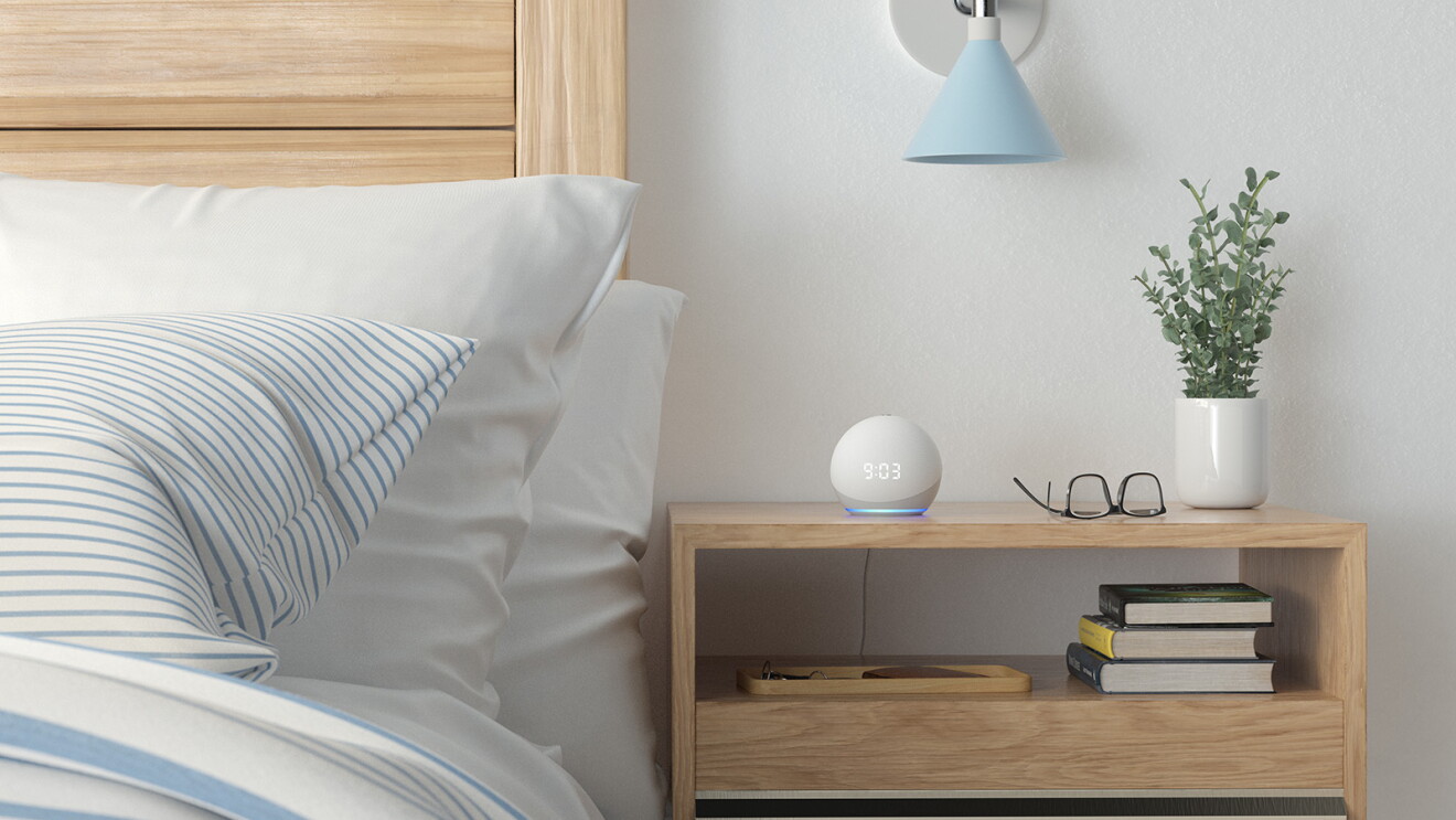 An Echo Dot device sits on a bedside table, displaying 9:03 as the time.