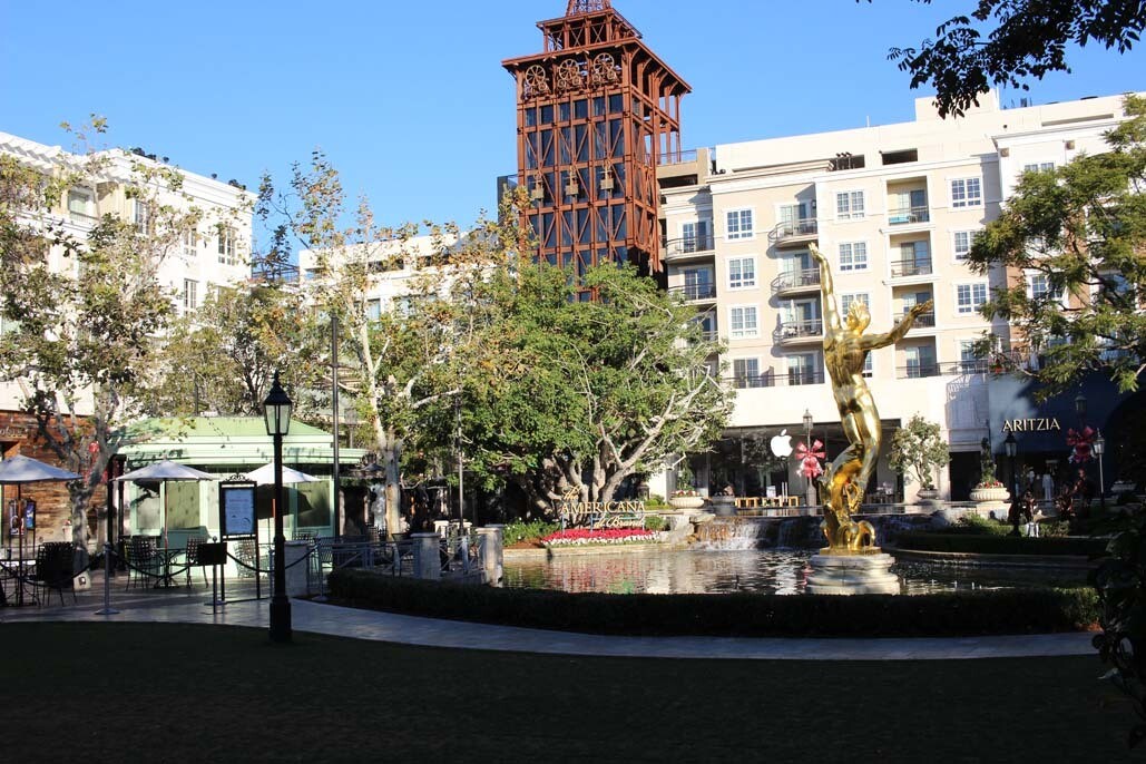 An image of a large fountain with a gold statue of a man in the middle. The fountain is in the middle of a mall with stores surrounding it.