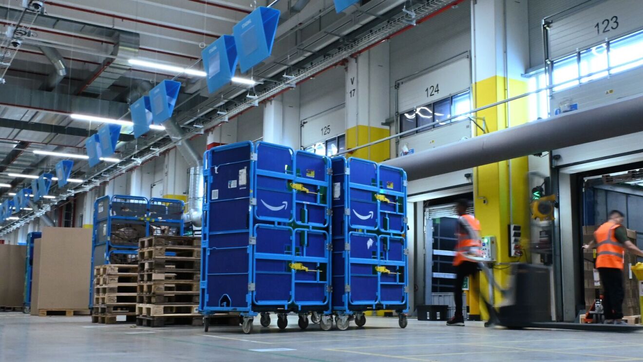 Logistikmitarbeiter stehen vor Öffnungen und großen blauen Karren.