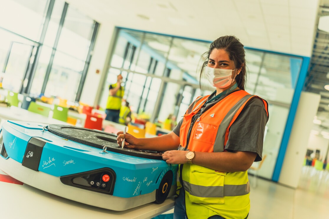 Eine Mitarbeiterin schreibt auf ein Amazon Drive ihren Namen. Neben ihr haben viele Kolleg:innen ebenfalls unterschrieben.