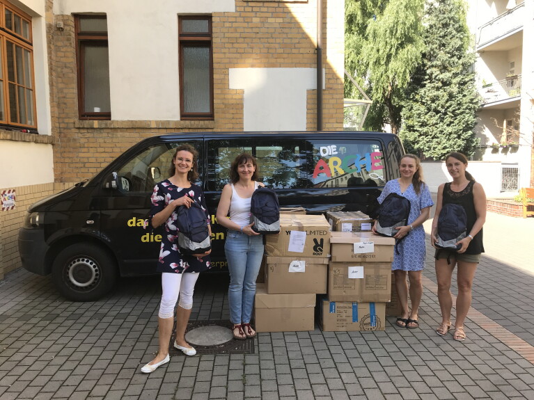 Volunteers von Amazon mit gespendetem Schulmaterial und Kisten vor einem Van der Arche.