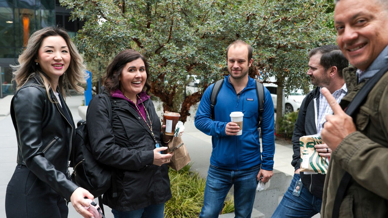 A photo of five employees standing outside of Amazon's Seattle headquarters holding cups of coffee.