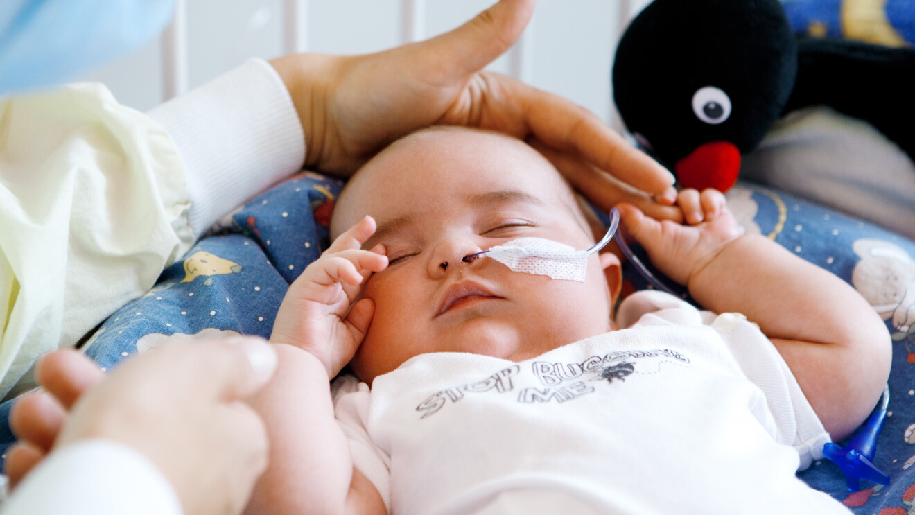 Eine Mutter legt schützend ihre Hand über den Kopf ihres kranken Babys