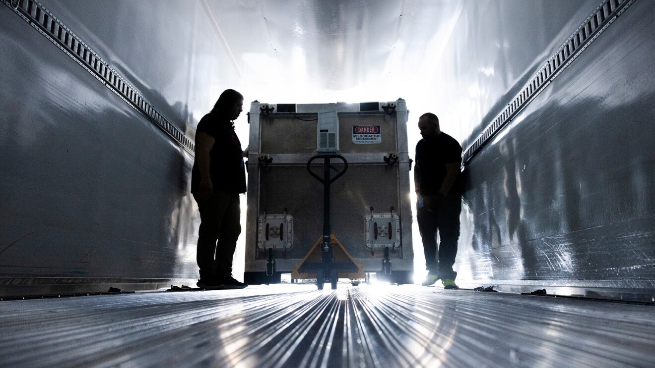 An image of two men pushing a Project Kuiper shipping container into a truck.