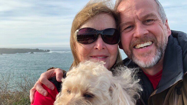 David, Cynthia and their dog smiling at the camera with the ocean in the background. 