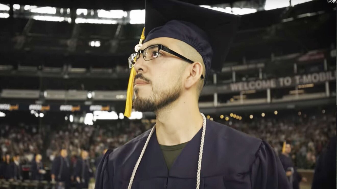 Julio wears a graduation cap and gown and looks up into the crowd.