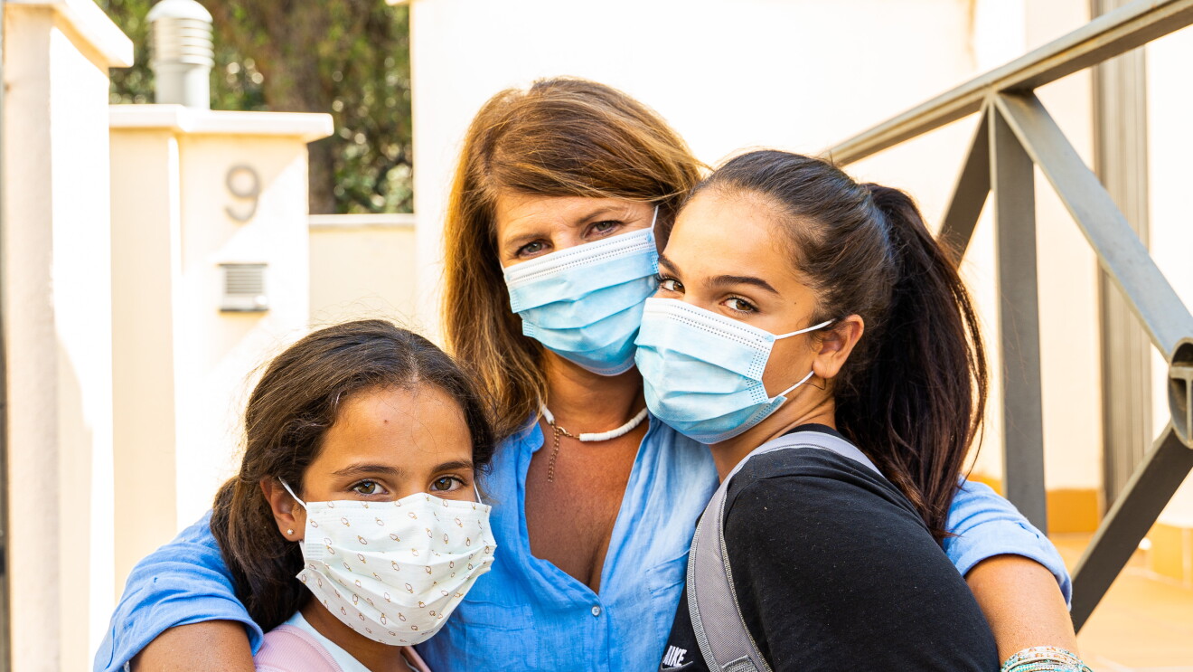 Gloria Santamaría con sus hijas Manuela de 13 años y Martina de 11. En el portal de su casa, con un muro de color blanco de fondo. Las tres van con mascarilla. Gloria en el centro de la foto agarra a sus dos hijas. Las tres miran a cámara. Tienen el pelo largo. Gloria castaño y las chicas de color negro. Además, están todas morenas. 