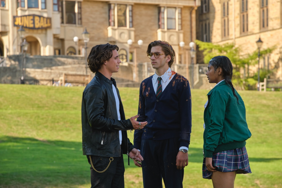 Three teenagers stand in a circle with a school in the background