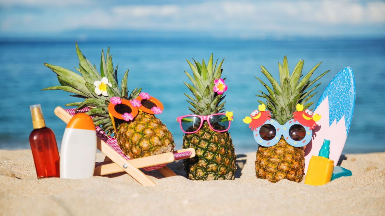 A trio of pineapples wearing sunglasses on the beach.