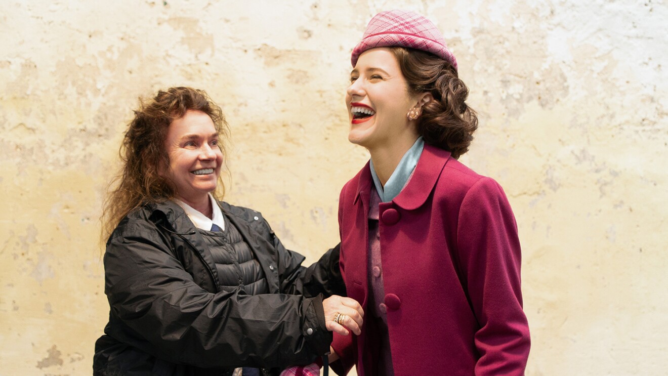 一个女人正在给一个女演员缝补一件戏服的形象。两人都在微笑和大笑。