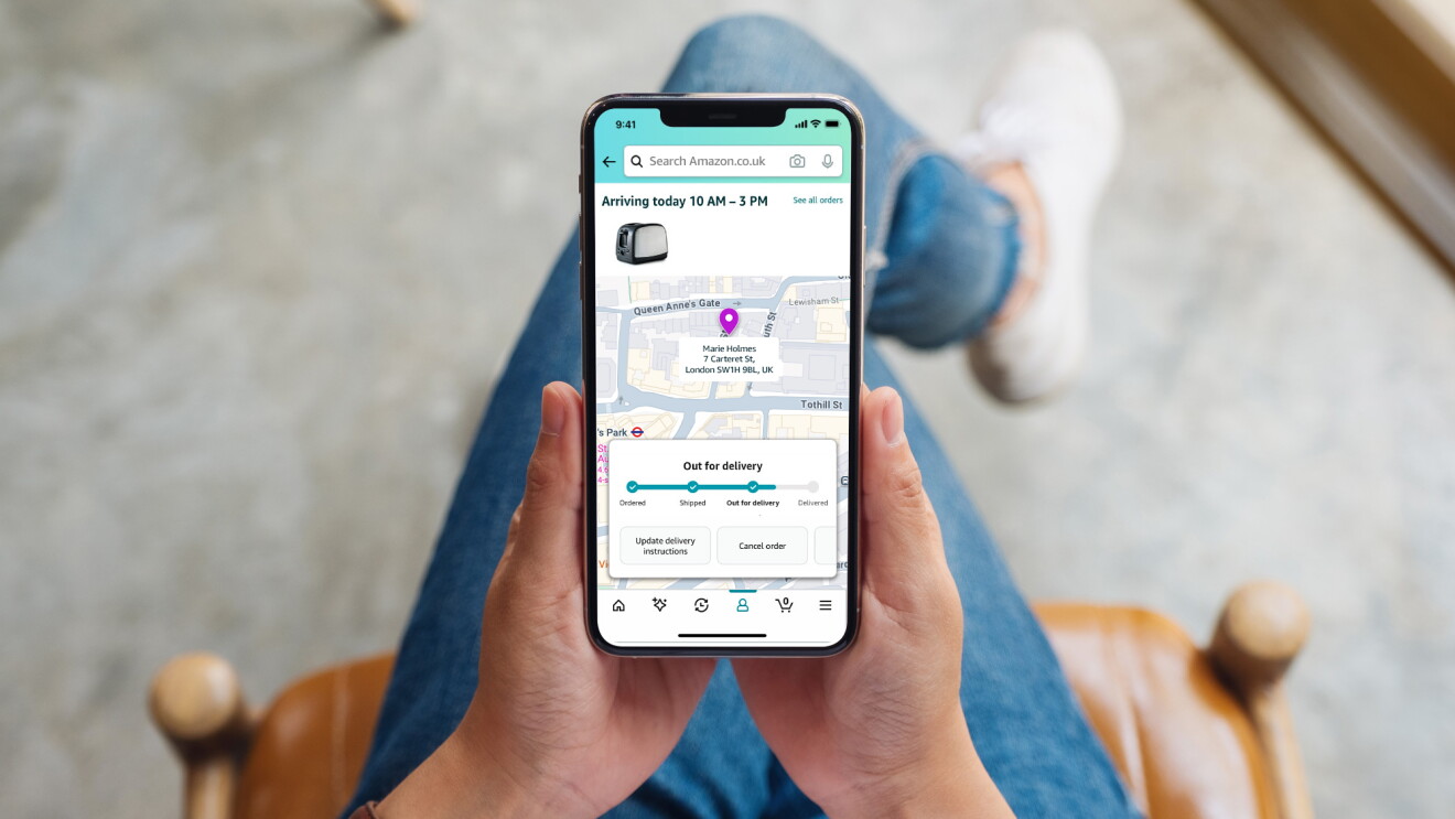 Someone holds a phone which displays a map where they are tracking the delivery of an Amazon package
