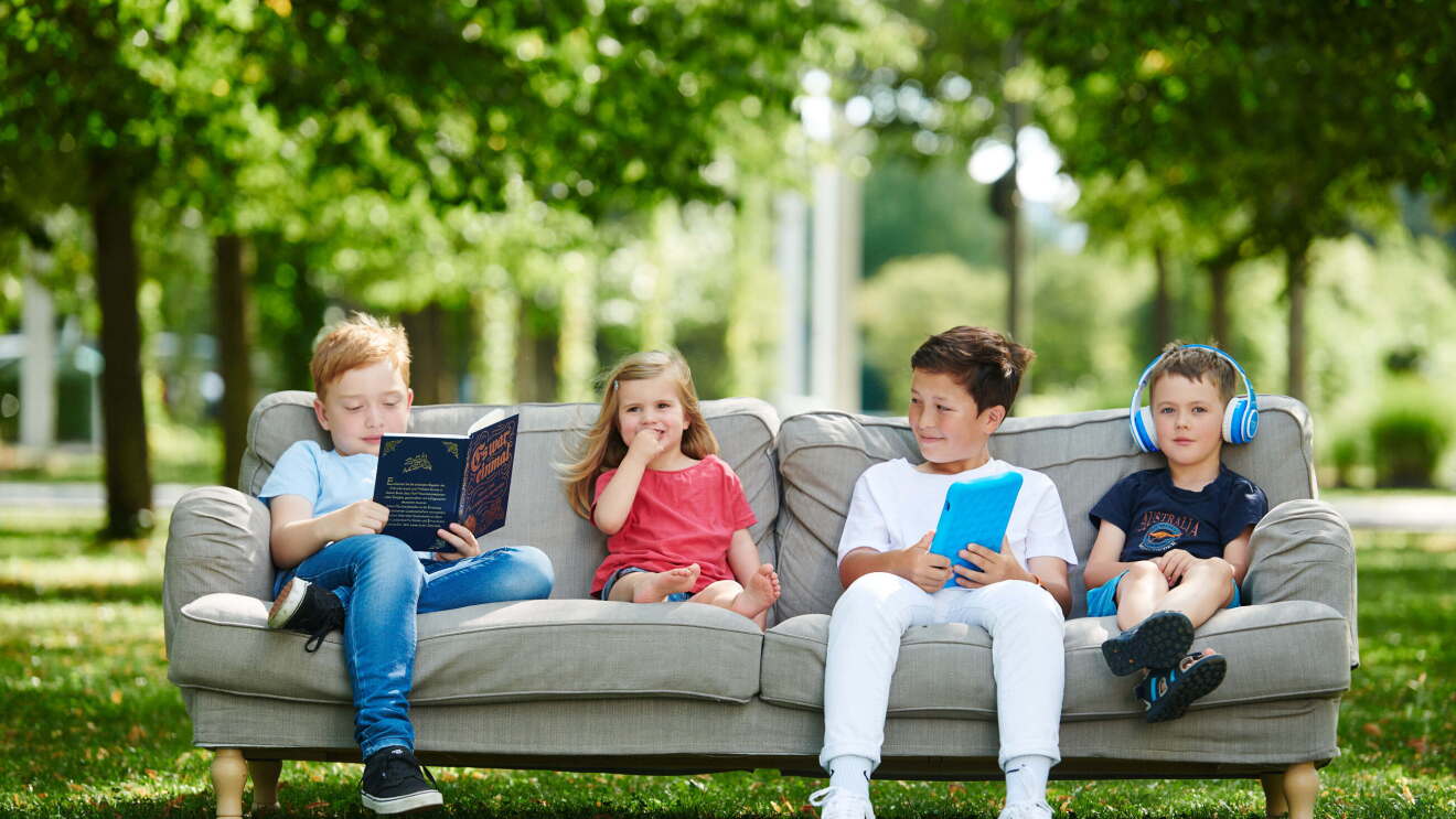 Kinder sitzen im Freien auf einer Couch und lesen Märchen