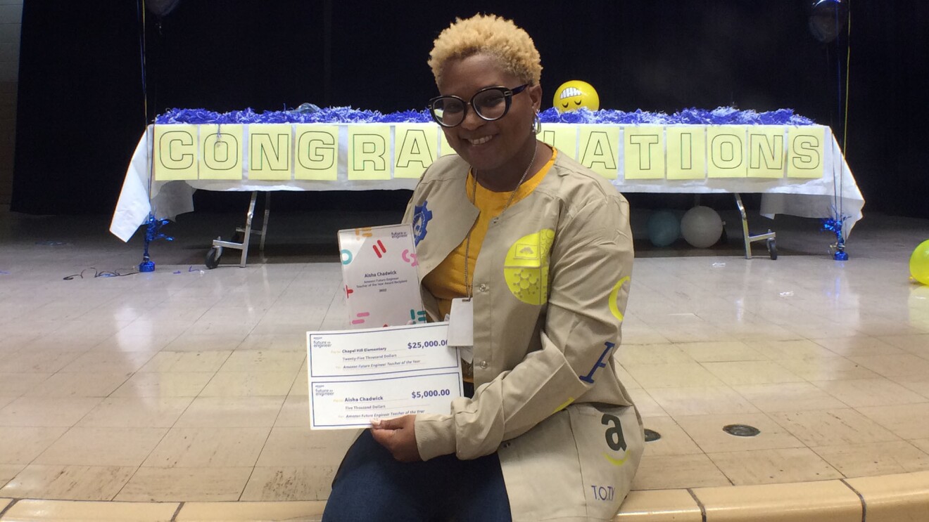 艾莎·查德威克(Aisha Chadwick)拿着她的获奖支票和气球,身后还有一个写着“祝贺”的牌子。