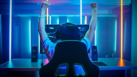 Gamer sitting on a chair in front of a monitor raising hands in victory