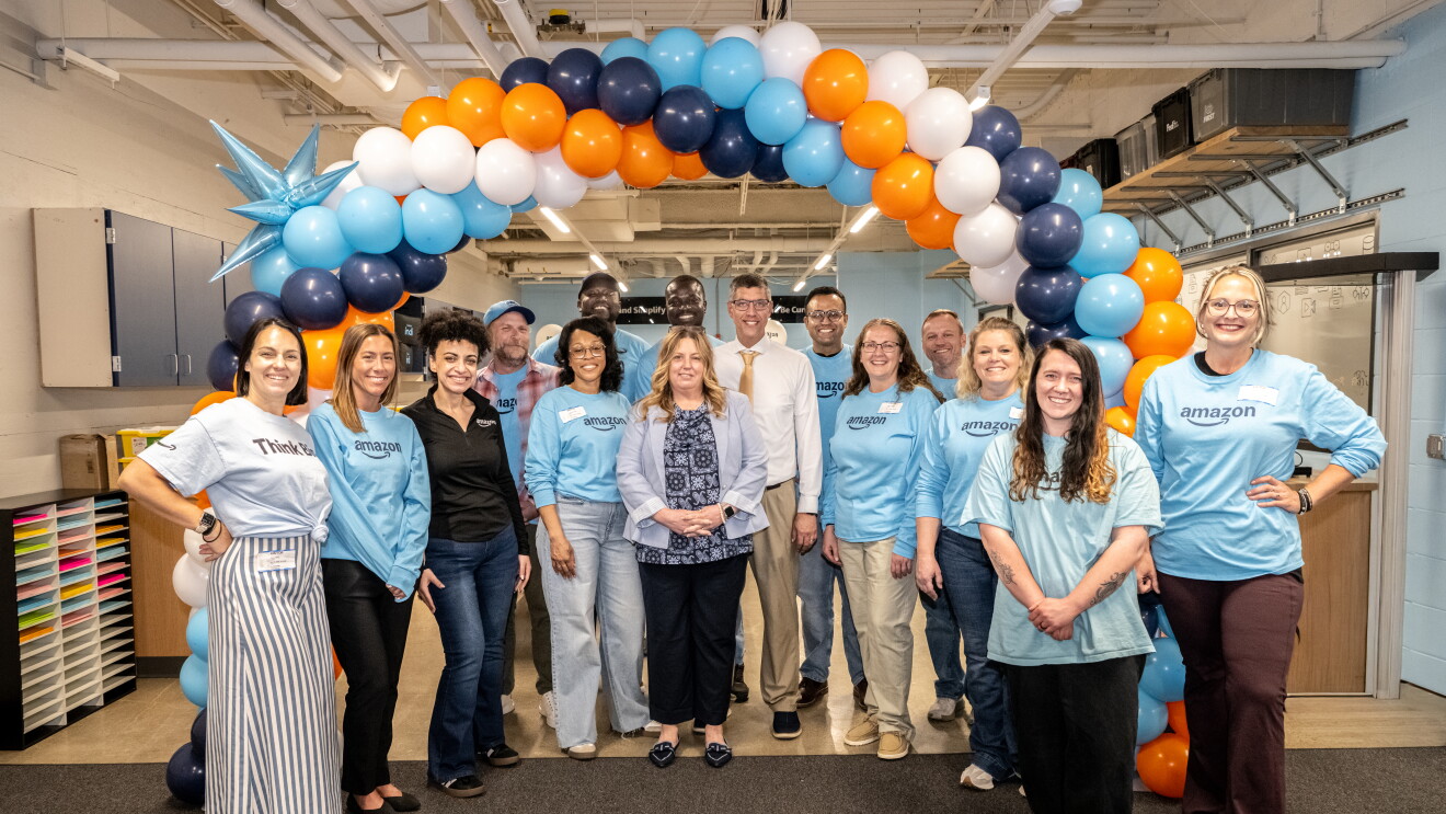 Amazon team members posing together under a colorful balloon arch in an office setting