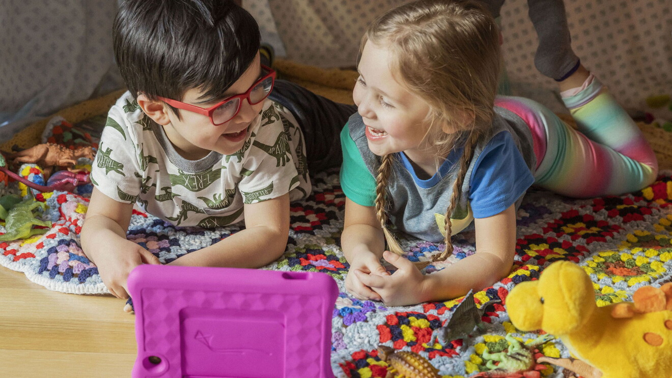 An image of two kids playing on the floor looking at an Amazon Kids tablet. 