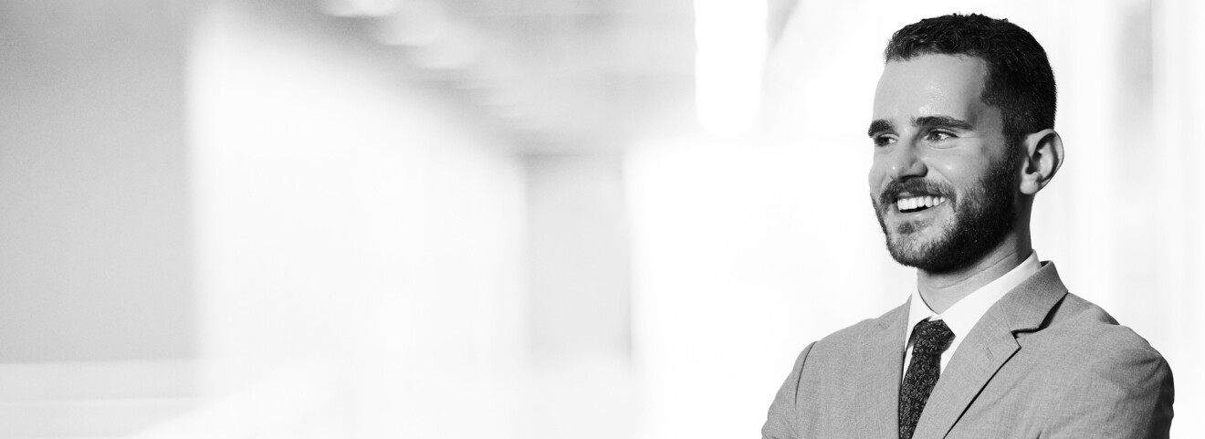 A headshot image of Russell Silver-Fagan. He is standing in a white hallway smiling for the photo.