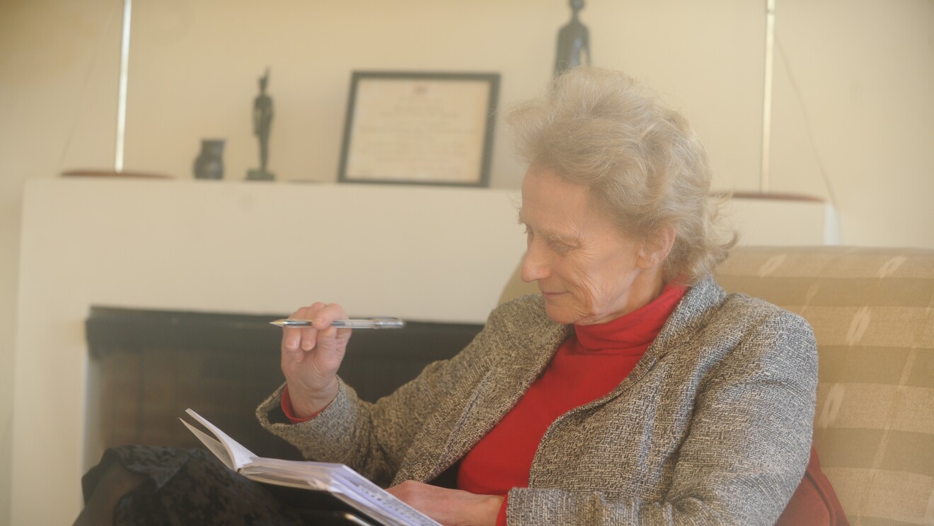 Dame Athene Donald is pictured sat on a sofa, holding a pen while looking into a notebook